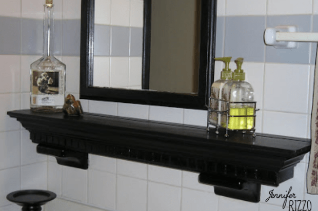 A black wooden shelf beneath a mirror holds a bottle, a small decorative object, and two soap dispensers in a caddy—no useless bathroom ceramic holders clutter this crisp white tiled wall.