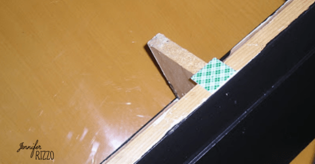 A piece of green-patterned tape secures a broken wooden frame joint on a black and wood surface, as ineffective as those useless bathroom ceramic holders.