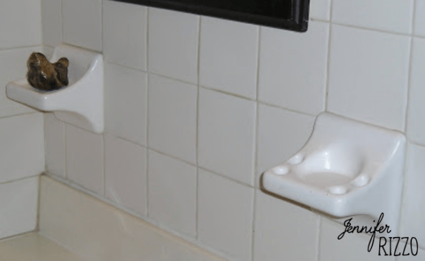 A white tile wall with useless bathroom ceramic holders and a sleek black frame.