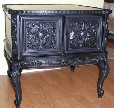 Ornate black wooden cabinet with carved doors and curved legs, featuring a stunning side table makeover with a decoupaged table top, placed on a wooden floor against a light-colored wall.