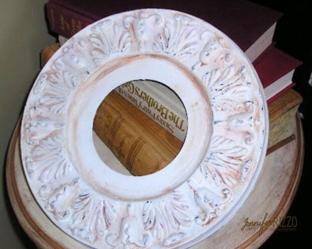 A decorative, round, white plaster medallion with ornate detailing rests on a wooden surface next to a stack of books.