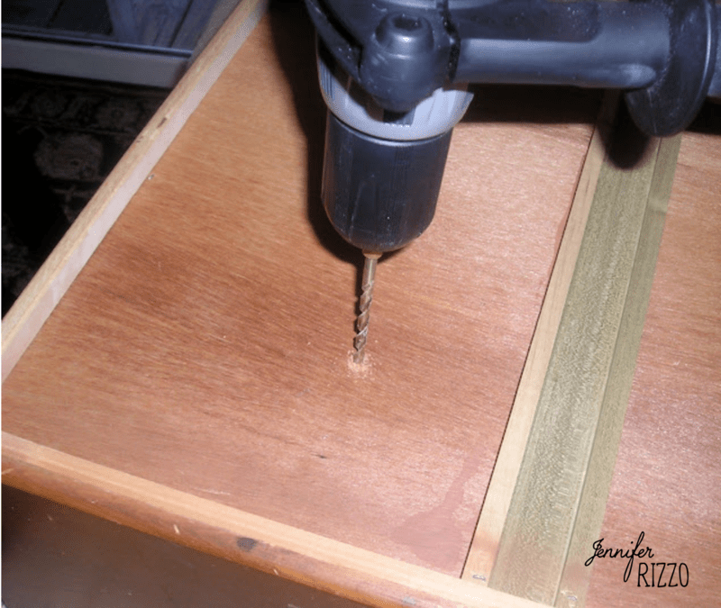A power drill with a drill bit is positioned to make a hole in a wooden drawer, transforming a repurposed dresser drawer into a planter.