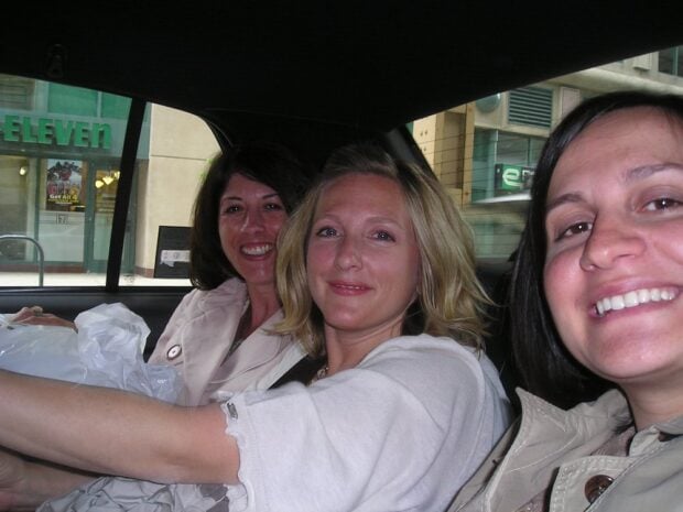 Three women are sitting together in the backseat of a car, smiling at the camera after attending a creative business conference with Country Living Magazine. A 7-Eleven store is visible through the window outside.