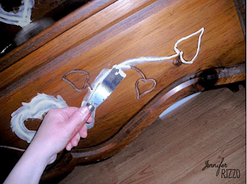 a hand Smoothing wood putty with a putty knife on filling in carved wood areas