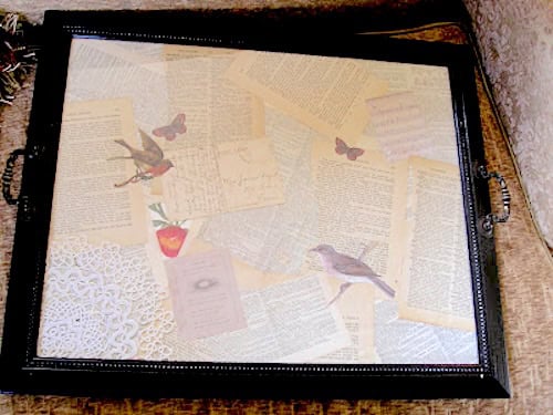 Turn a picture frame into a decorative tray with black handles, featuring a collage of vintage book pages, butterflies, birds, a strawberry, and delicate lace on its surface.