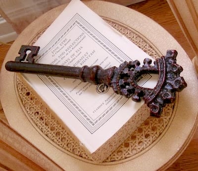 A large, ornate antique key rests on top of a closed book with a decorative cover—perfect inspiration for the removal of covers from books for decorating—placed elegantly on a woven surface.