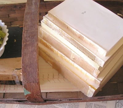 A stack of books with plain covers and visible aged edges, created by the removal of covers from books for decorating, is arranged in a wooden tray.