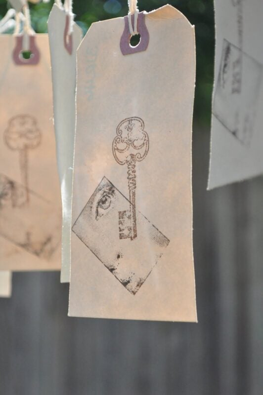 A cream-colored tag with a stamped image of a vintage key and a geometric shape containing a partial eye, hanging by a string—perfect for making DIY tea-dyed tags with an artistic twist.
