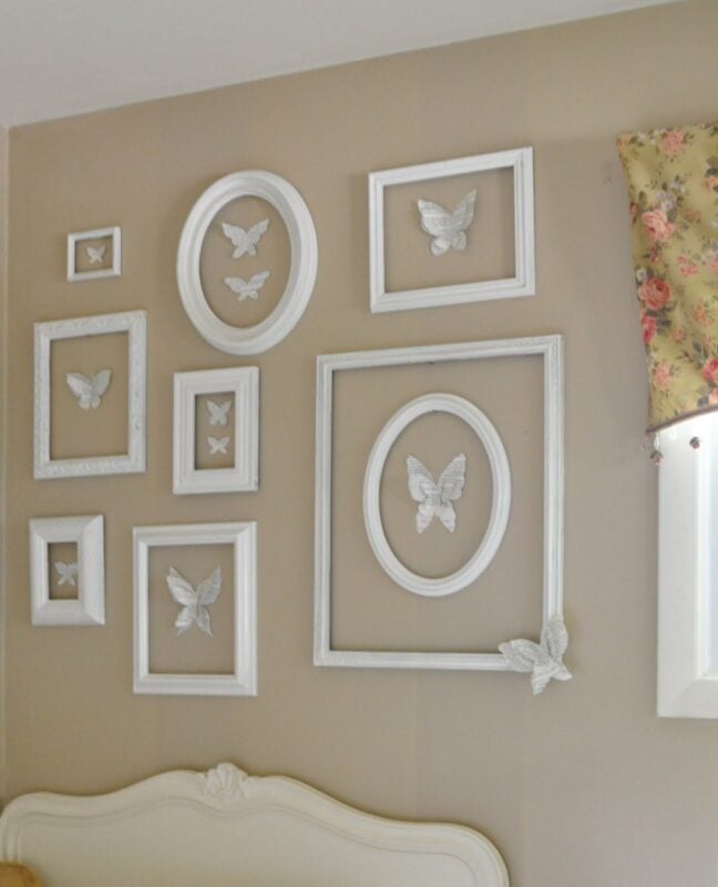 A beige wall in this butterfly-inspired girl's bedroom displays white picture frames of various sizes, each containing a white butterfly decoration, arranged in an asymmetrical pattern.