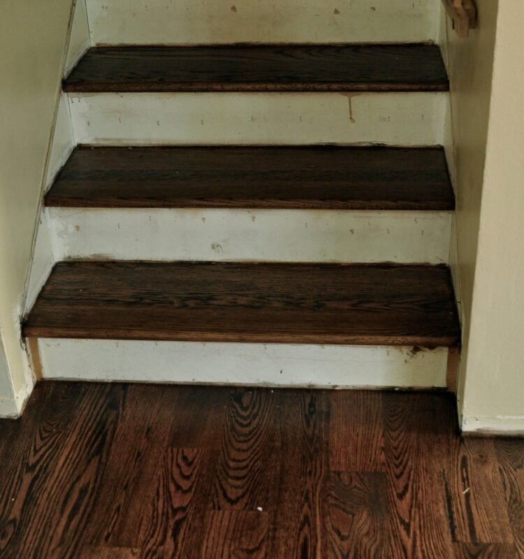 A close-up view of a stairway with dark stained treads and white risers, showing some scuff marks and signs of wear—perfect inspiration for a staircase makeover.