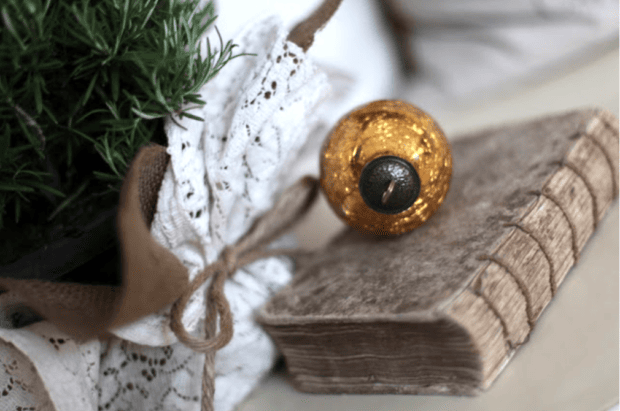 A vintage book with a worn cover sits beside a gold ornament and a bundle wrapped in lace and twine, creating a charming scene inspired by Holiday Housewalk 2011 Day 2 traditional holiday decor.