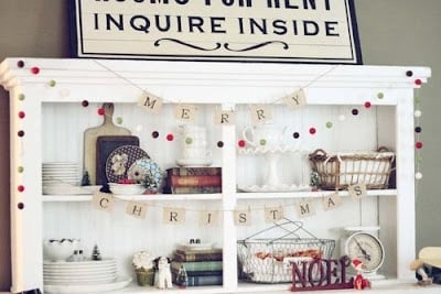 A white hutch decorated with Christmas garland, dishes, books, and holiday ornaments captures the festive spirit of a Holiday housewalk, with a "ROOMS FOR RENT" sign placed on top.