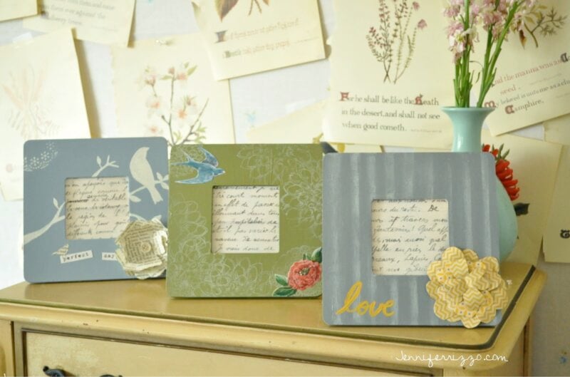 Three decorated picture frames from the Sparrow and Blossom Collection, adorned with floral designs and handwritten notes, rest on a beige dresser. Papers and botanical prints decorate the wall in the background.