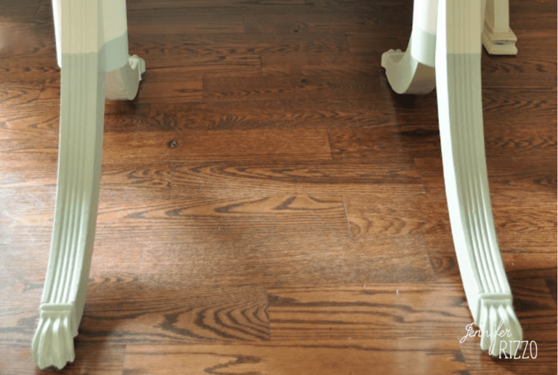 Table legs with claw feet rest on a reddish-brown hardwood floor, their lower sections featuring a Dip Dye Paint Technique in a light color for a stylish contrast.