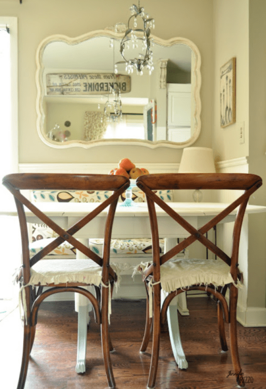 Two wooden chairs with cushions sit at a white table in front of a large mirror, while the lamp and decorative items showcase the Dip Dye Paint Technique for added style.