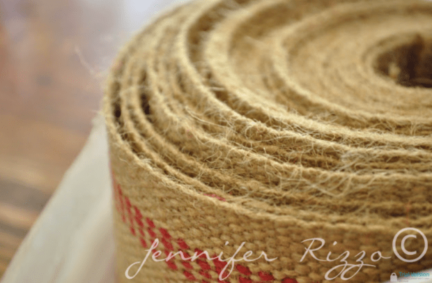 A close-up of a rolled jute or burlap ribbon with a red stripe, perfect for adding rustic charm to your next luggage rack makeover, placed on a white surface.