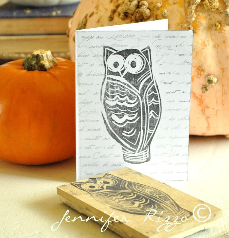 A greeting card with a black owl illustration stands next to a matching owl stamp—perfect inspiration if you want to carve your own rubber stamps—with two pumpkins in the background.