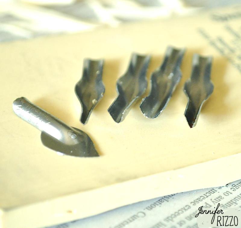 Five metal rubber stamp carving blades are arranged on a light surface, with one nib separated from the group—perfect tools to carve your own rubber stamps. The name "Jennifer Rizzo" is visible in the bottom right corner.