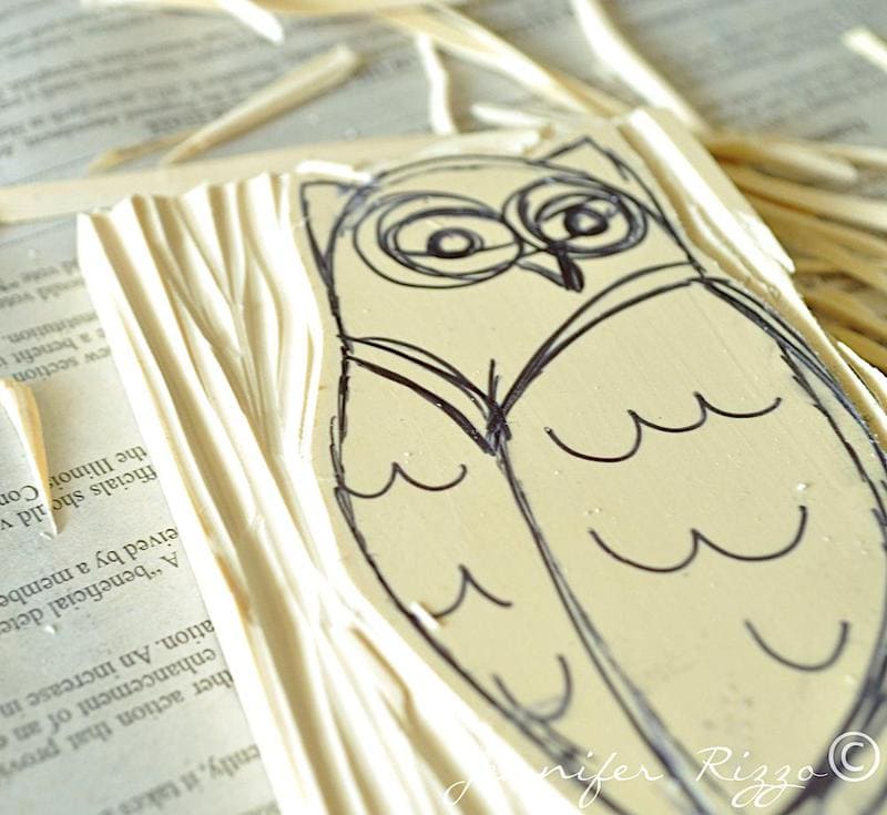 A hand-drawn owl sketch on a linoleum block with carved lines, resting on an open book—inspiring you to carve your own rubber stamps.
