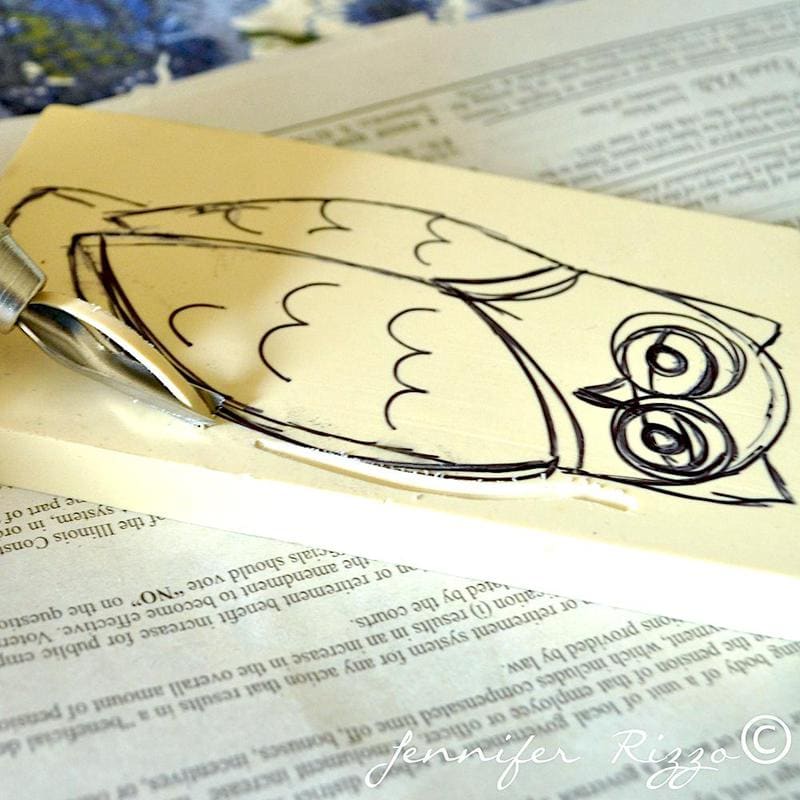 A carving tool outlines an owl drawing on a piece of linoleum, with an open book underneath—perfect inspiration if you want to carve your own rubber stamps. “Jennifer Rizzo©” is written on the image.