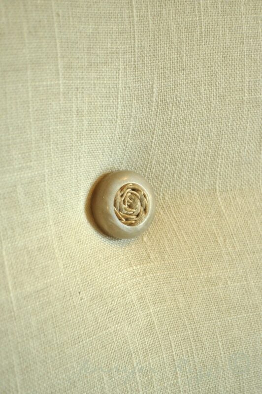 Close-up of a beige fabric surface with a single round decorative button tufted into it, perfect for modernizing an old cane back chair with tufting.