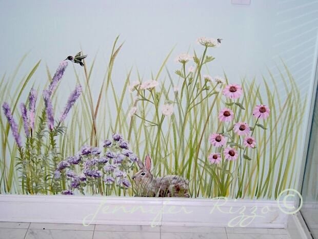 A painted wall mural depicting wildflowers, tall grass, a hummingbird, a bee, and a rabbit, with a signature at the bottom.