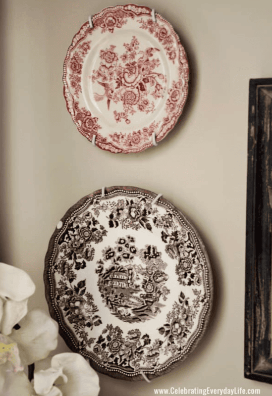 Two decorative vintage plates with intricate floral patterns hang on a beige wall—one with red designs, the other with black—perfect for decorating a powder room with timeless charm.
