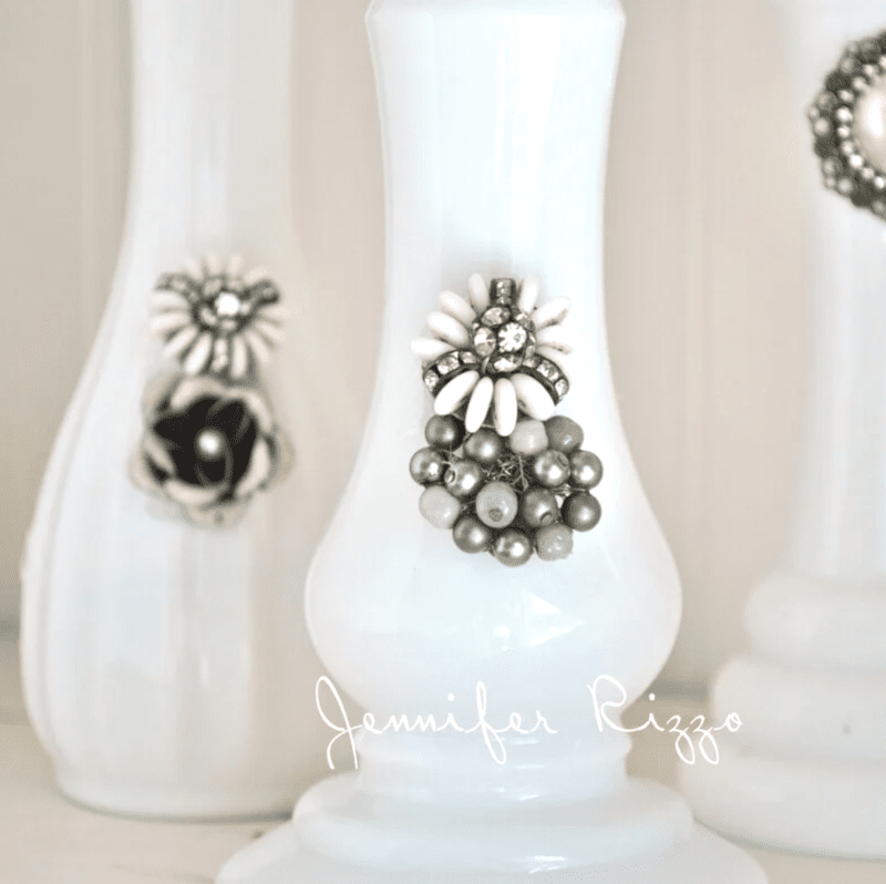 Three white vases upcycle milk glass vases with broken jewelry, adorned with vintage-style brooches featuring pearl-like beads and rhinestones. "Jennifer Rizzo" is written across the bottom.