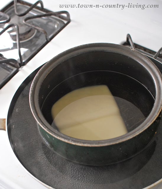 A double boiler sits on the stovetop, its pot filled with water and a block of beeswax gently melting to craft lavender scented candles.