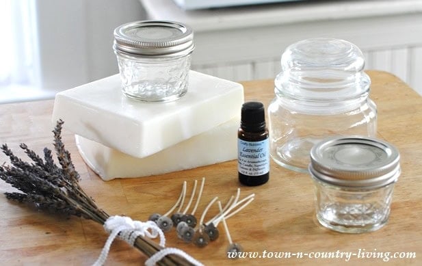 Soap-making ingredients: bars of soap base, glass jars, an essential oil bottle, wicks, and dried lavender arranged on a wooden surface—perfect for crafting soothing lavender scented candles.