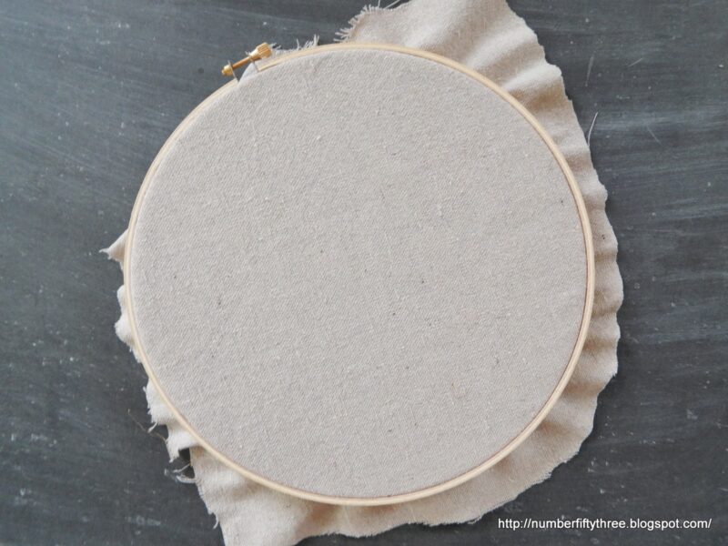 An embroidery hoop with plain fabric secured tightly, positioned on a dark surface—perfect for an easy DIY beginner embroidery project.