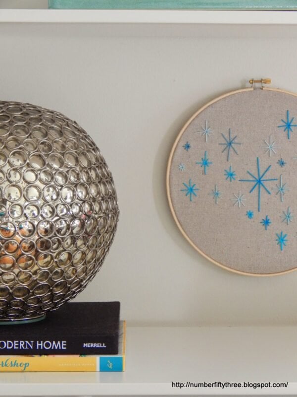 A decorative metal orb sits on stacked books beside an embroidered hoop, showcasing a blue star pattern—an easy DIY beginner embroidery project that brightens up any shelf.