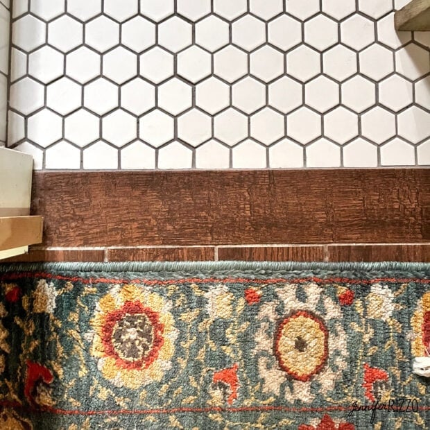 A section of floor features hexagonal white tiles, a strip of wood look ceramic tile flooring, and a colorful patterned rug with red, yellow, and green designs.