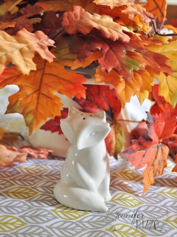 Part of the fall home tour, a ceramic fox figurine perches on a geometric-patterned surface, adorned with autumn leaves in vivid shades of orange and yellow.