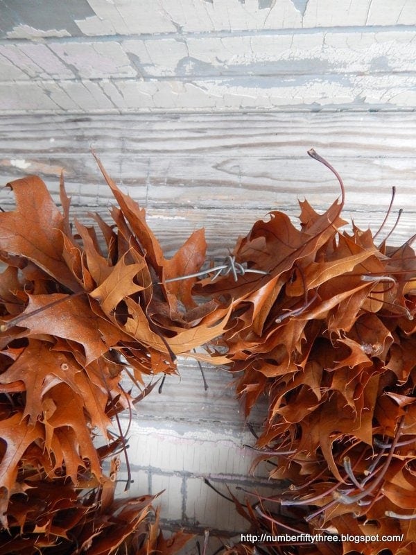 A close-up of an oak leaf wreath made of dried brown leaves hanging on a wooden wall with peeling paint.