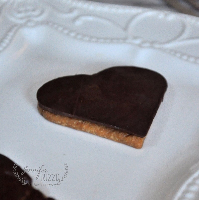 A heart-shaped cookie with a chocolate coating, resembling delectable pie crust cookies, sits elegantly on a decorative white plate.
