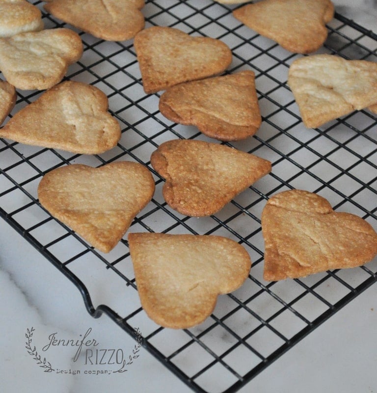 A cooling rack with golden-brown, heart-shaped cookies made from pie crust cookies evenly spaced across it. The cookies are of varying shades, indicating they were baked in batches.