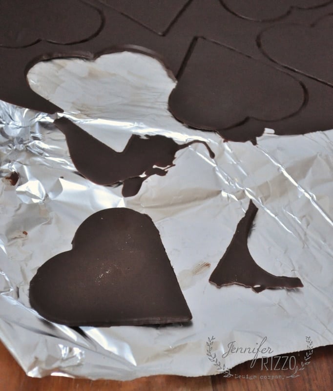 Chocolate heart shapes on aluminum foil, with some cut-out sections missing, resemble the playful creativity of pie crust cookies.