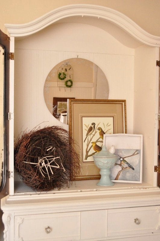 White cabinet with bird-themed framed art, a round mirror, a decorative twig nest, and a ceramic dish holding a small white bird figurine—an inspiring example of furniture makeovers before and after.