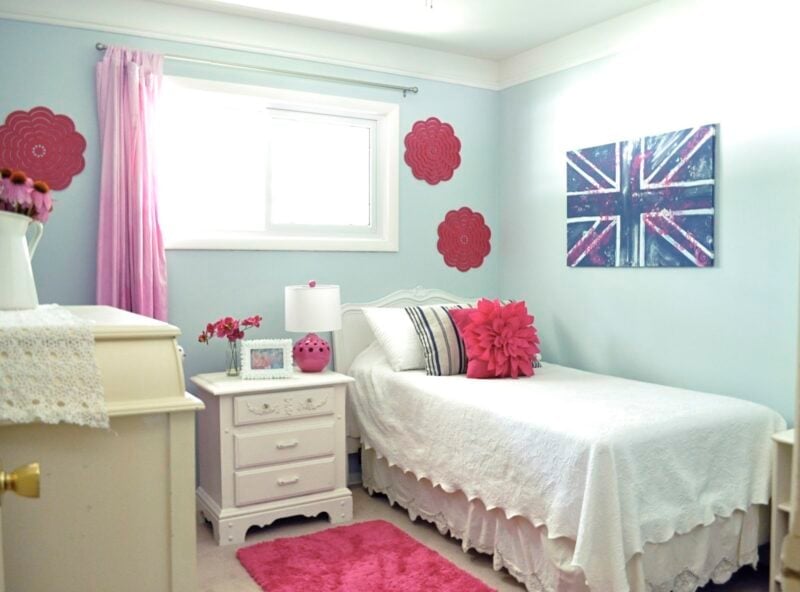 A neatly arranged guest room makeover featuring a single bed, white furniture, pink decor accents, and a Union Jack artwork on the wall.