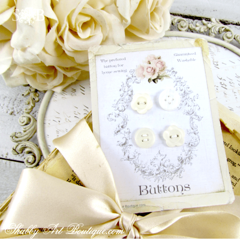 Four small white sewing buttons on a vintage-style display card, accented with a silk ribbon and cream-colored silk roses—a charming touch for any vintage button craft.