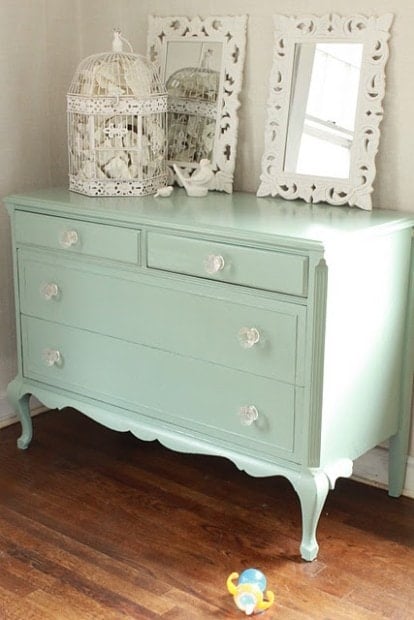 A mint green dresser, embodying the mint color trend, features two mirrors and decorative birdcages on top.