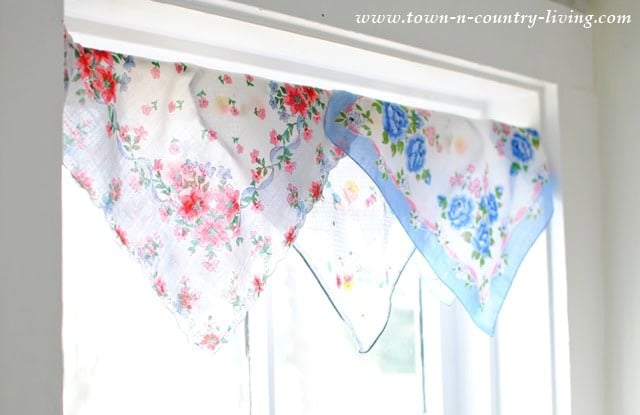 Vintage handkerchiefs with floral patterns are draped across the top of a window, serving as a charming decorative valance.Upcycling Vintage Handkerchiefs In Everyday Decor