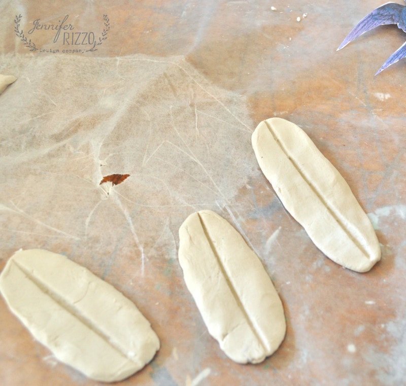 Three oval-shaped pieces of clay with a line down the center are arranged on wax paper, ready to become part of a DIY clay bird and feather wall hanging.