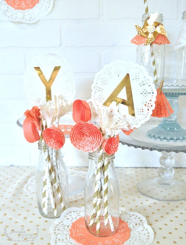 Two glass bottles with paper straws, coral paper flowers, and a Doily Paper Party Banner featuring gold "Y" and "A" letters decorate the festive table.