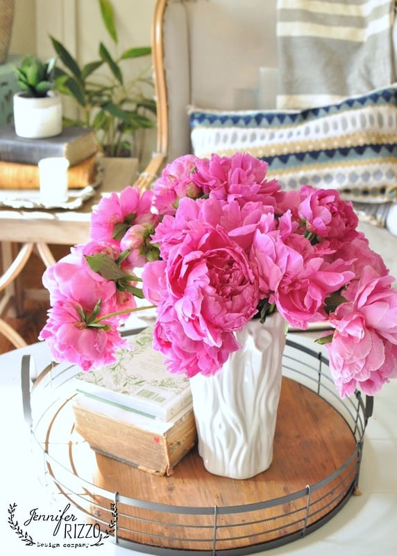 A bouquet of bright pink peonies in a white textured vase sits on a wooden tray with books, adding charm to this inviting split level home.