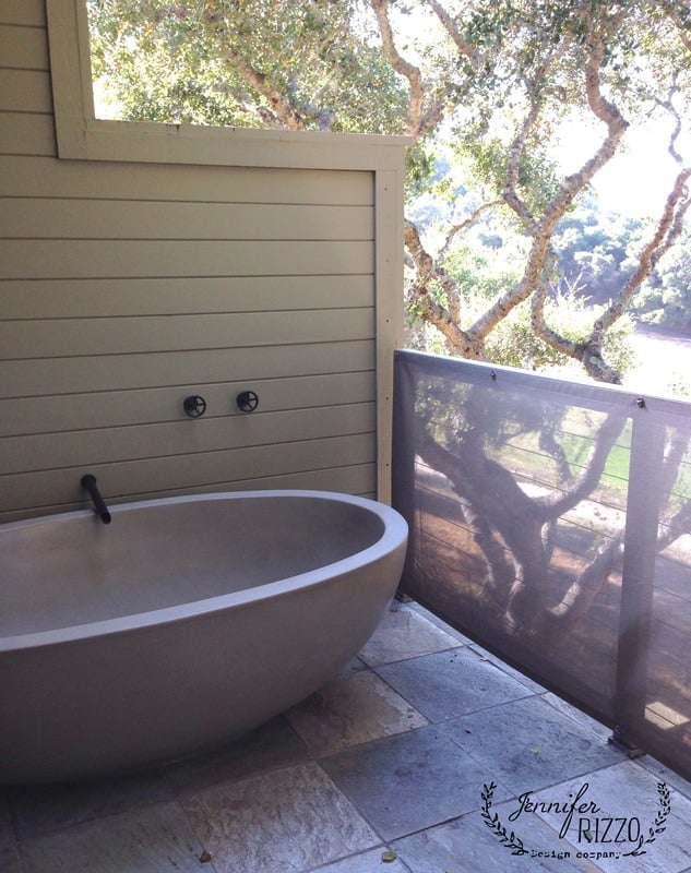 A standalone bathtub sits on an outdoor deck at Carmel Valley Ranch, framed by a wooden wall and surrounded by trees. The deck features a transparent mesh screen. The image includes a decorative stamp saying "Jennifer RIZZO design company.