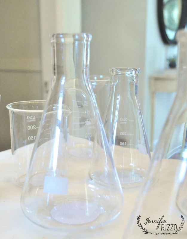 Clear glass laboratory beakers and flasks are placed together on a white surface, their measurement markings visible on the sides—perfect props for creating a creepy mad scientist Halloween laboratory scene.