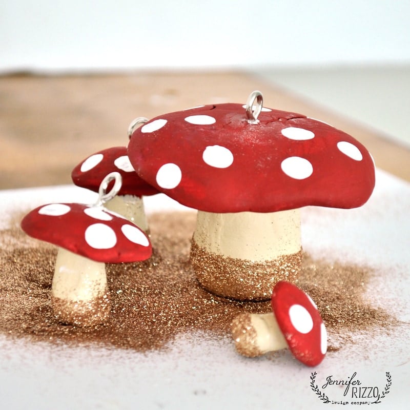 Three handcrafted clay mushroom ornaments with red caps and white spots, accented with gold glitter on the stems, bring a whimsical touch inspired by the holiday book Creatively Christmas, displayed beautifully on a flat surface.
