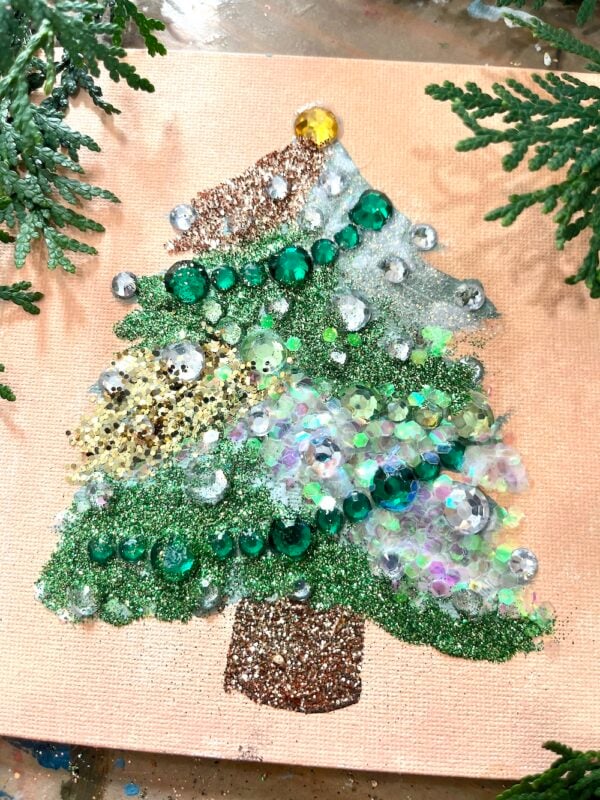 A bejeweled Christmas tree decoration, handmade with green and silver glitter, sequins, and beads on beige canvas, is beautifully accented by tree branches around the edges.
